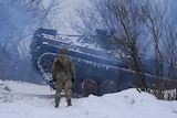 An Ukrainian serviceman stand by as an armored personnel carrier maneuvers in the snow.