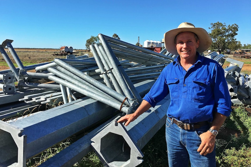 A man stands in front of a collection of scrap metal on a farm.