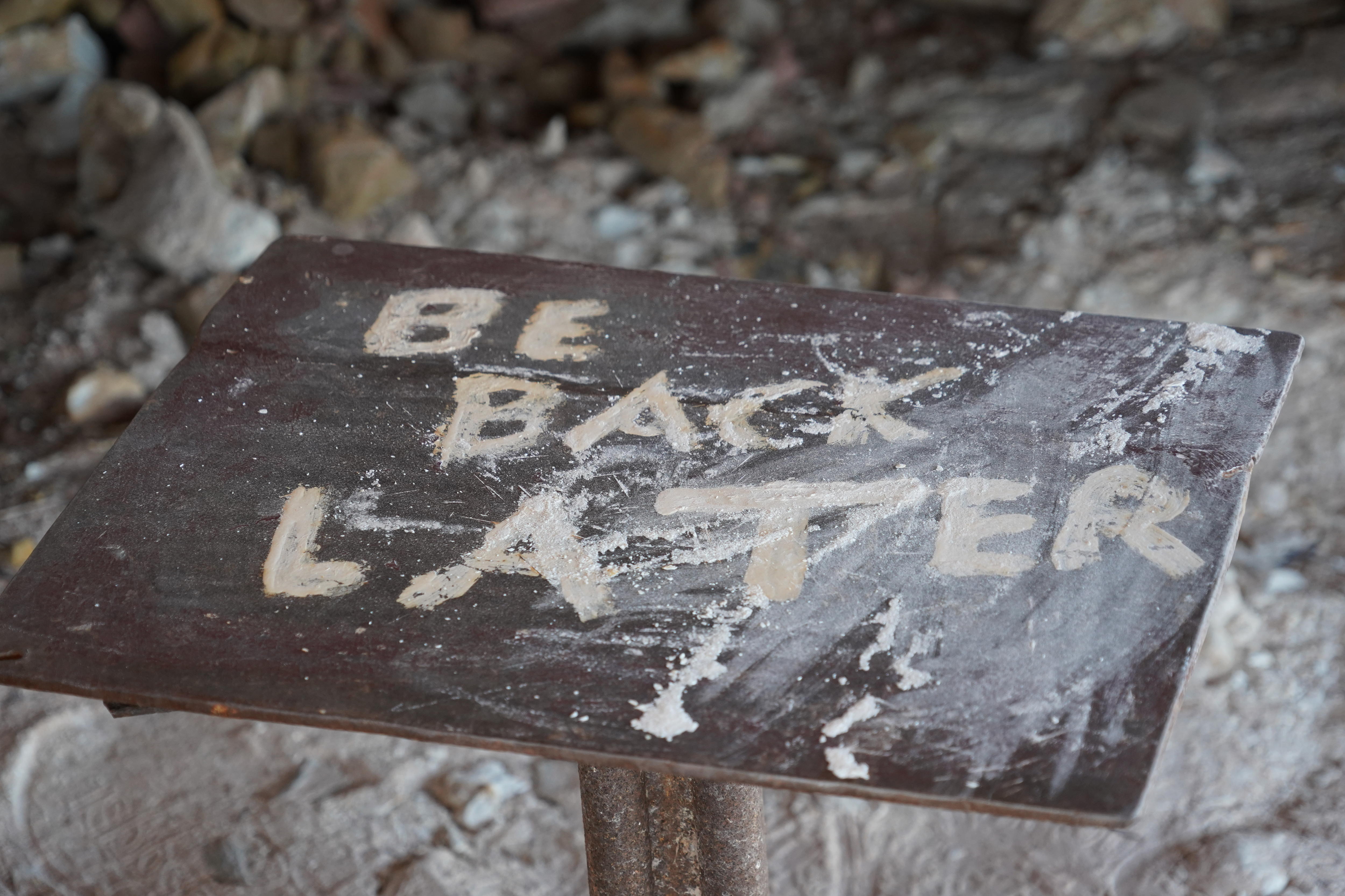 Un cuadrado de metal cubierto de polvo blanco con las palabras BE BACK LATER grabadas. 
