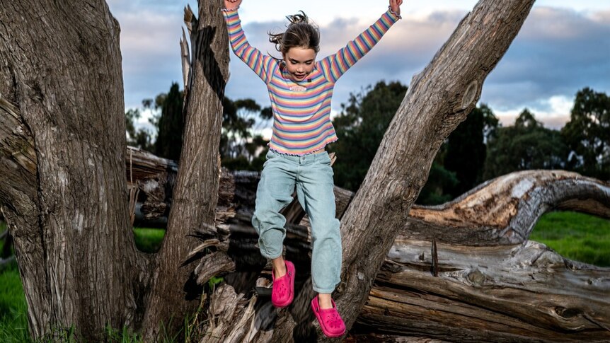 A young girl jumps from a fallen tree trunk.