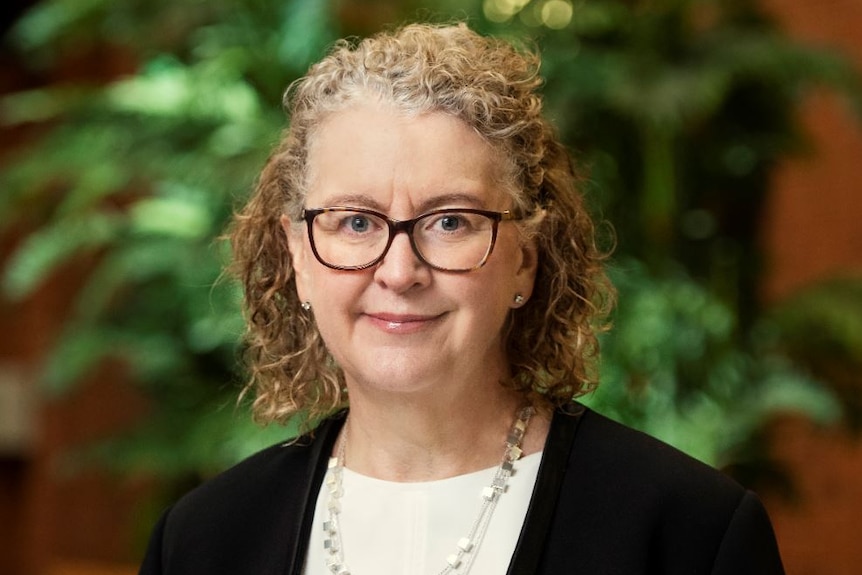 A blonde woman with curly hair and glasses looking at the camera and smiling