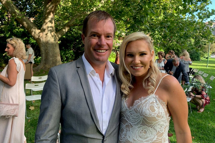 A man in a suit and a woman in a white dress smiling for the camera.