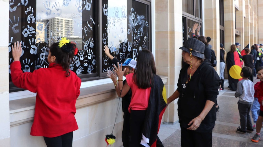 A group of children leave white handprints on the windows of Parliament House.