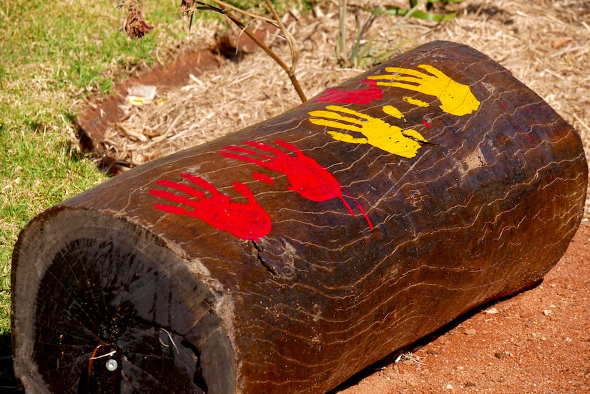 A wooden seat with red and yellow painted handprints on it. 