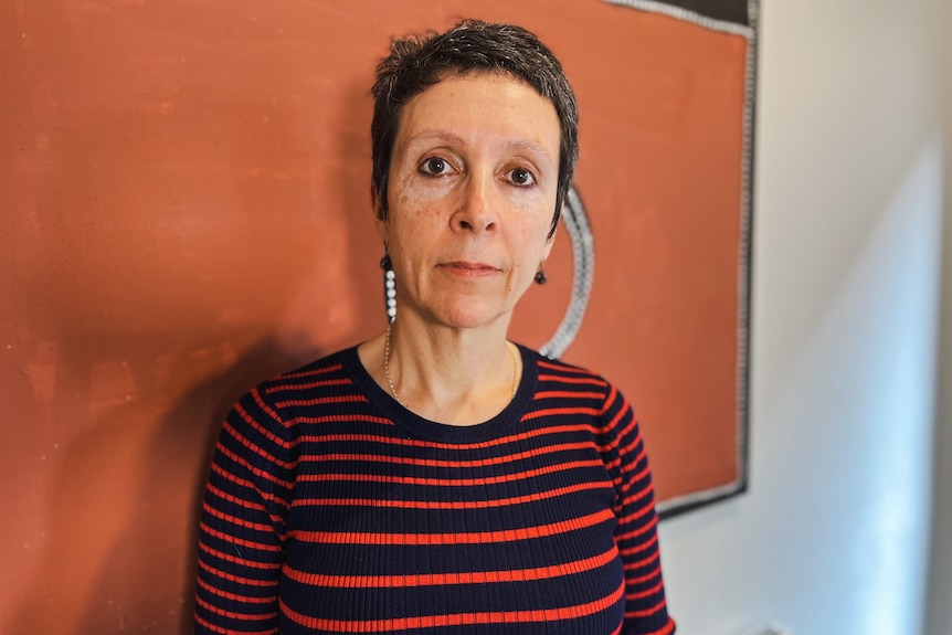 A woman in a orange and black striped shirt standing in an office, in front of an orange wall.