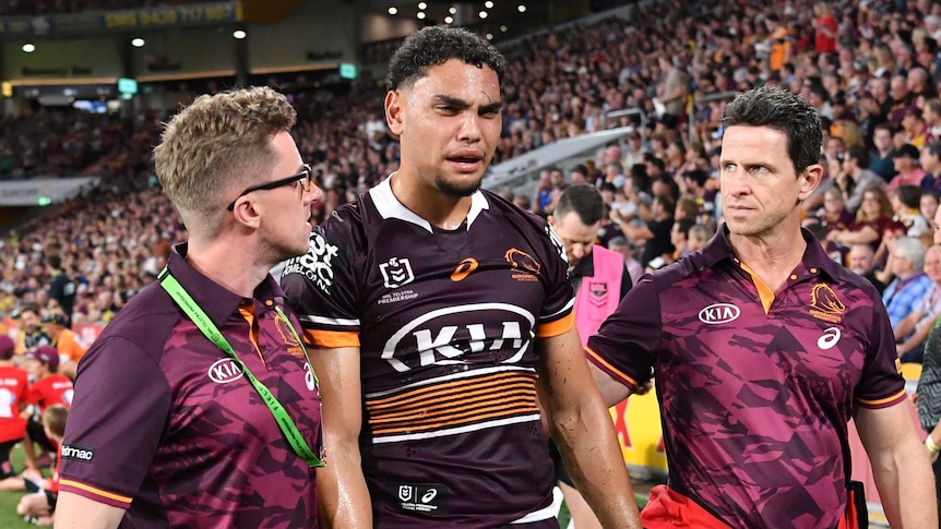 Brisbane Broncos player Xavier Coates is helped from Lang Park by trainers.