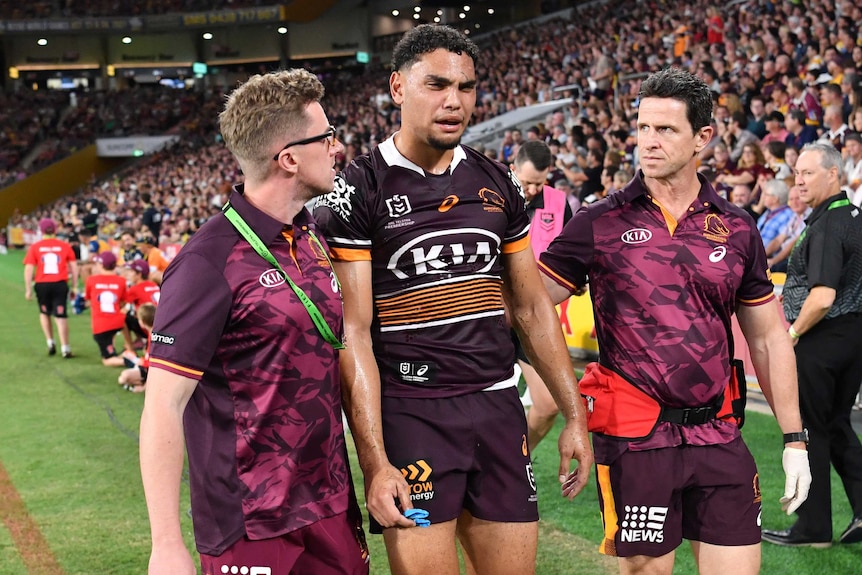 Brisbane Broncos player Xavier Coates is helped from Lang Park by trainers.