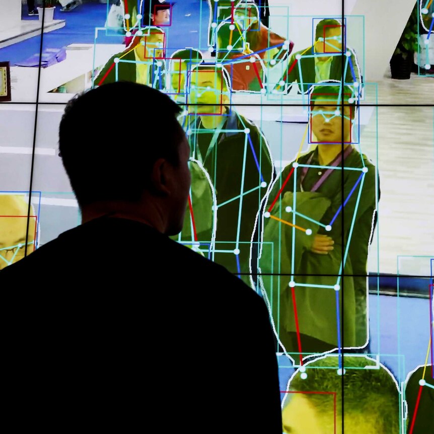 A man looks at a demonstration on a big screen of software tracking the movement of people.