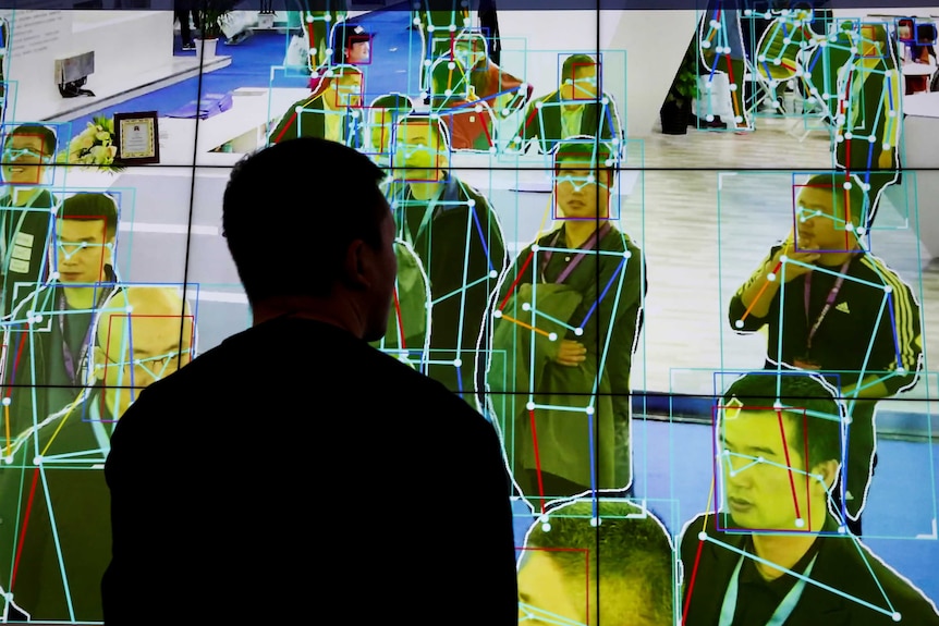 A man looks at a demonstration on a big screen of software tracking the movement of people.