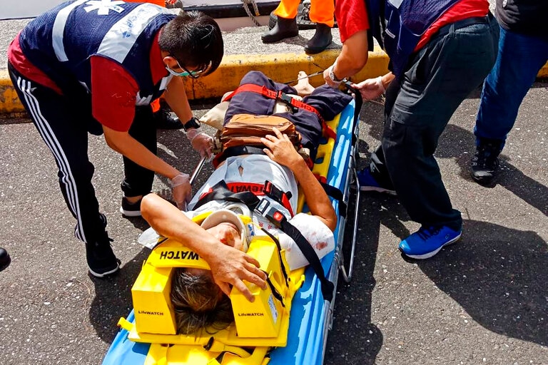 several rescue team members in orange and blue assisting an injured victim on a stretcher