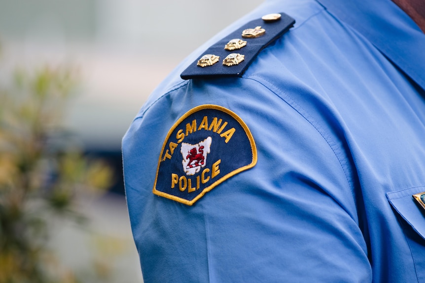 Blue and orange fabric badge on a blue shirt reads: Tasmania Police