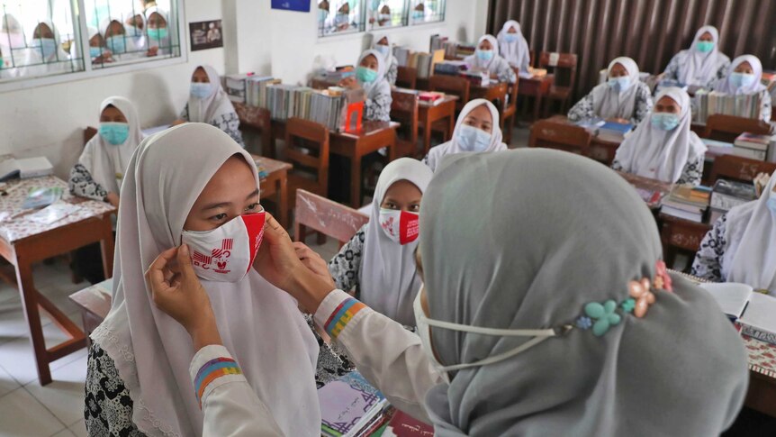 A public health official shows how to properly wear face masks to students