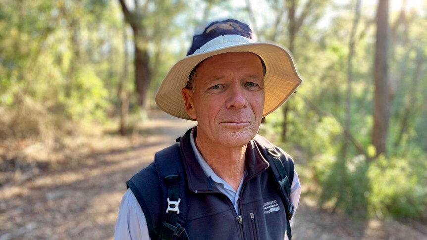 Ted Woodley standing on a walking track in the bush wearing a sun hat and hiking clothes