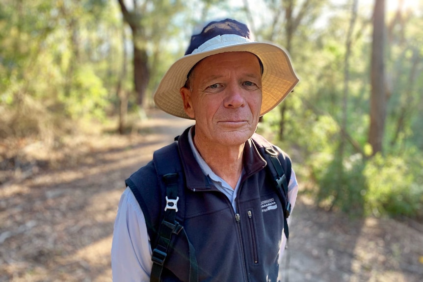 Ted Woodley standing on a walking track in the bush wearing a sun hat and hiking clothes