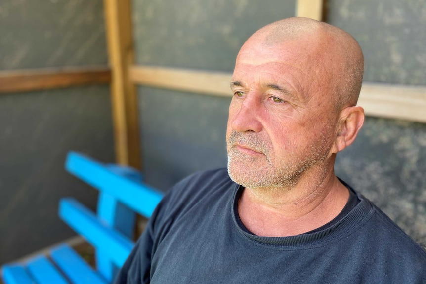 A man sits at a bus stop and stares into the distance.