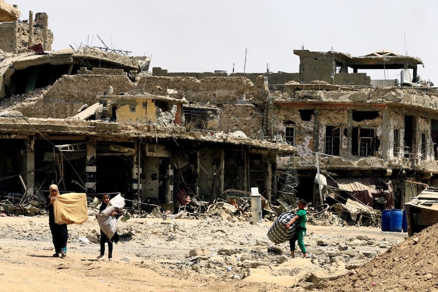 Civilians carry their belongings as they walk between destroyed buildings by clashes in the Old City of Mosul.