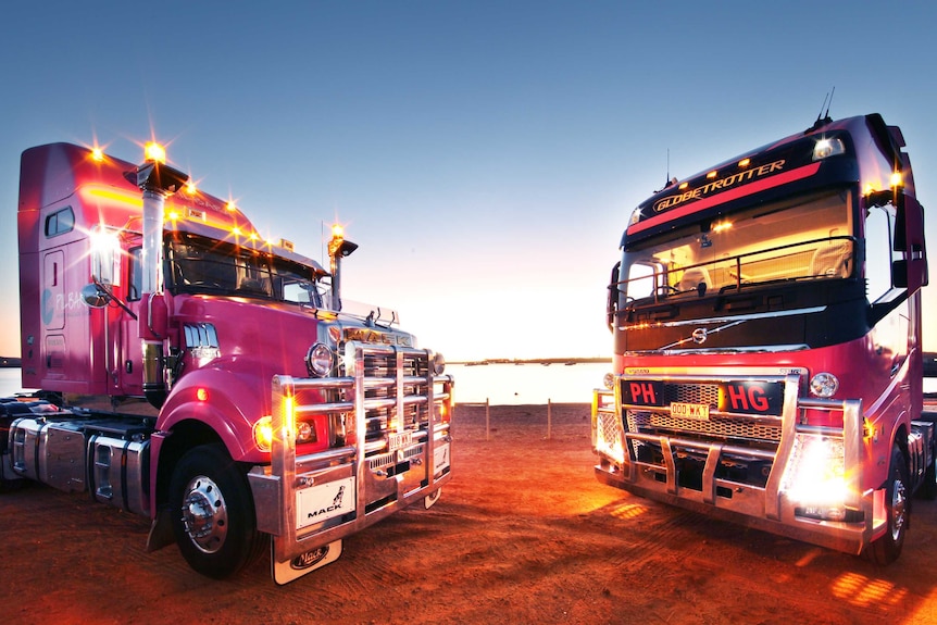 Two pink trucks face each other at sunset in the outback.