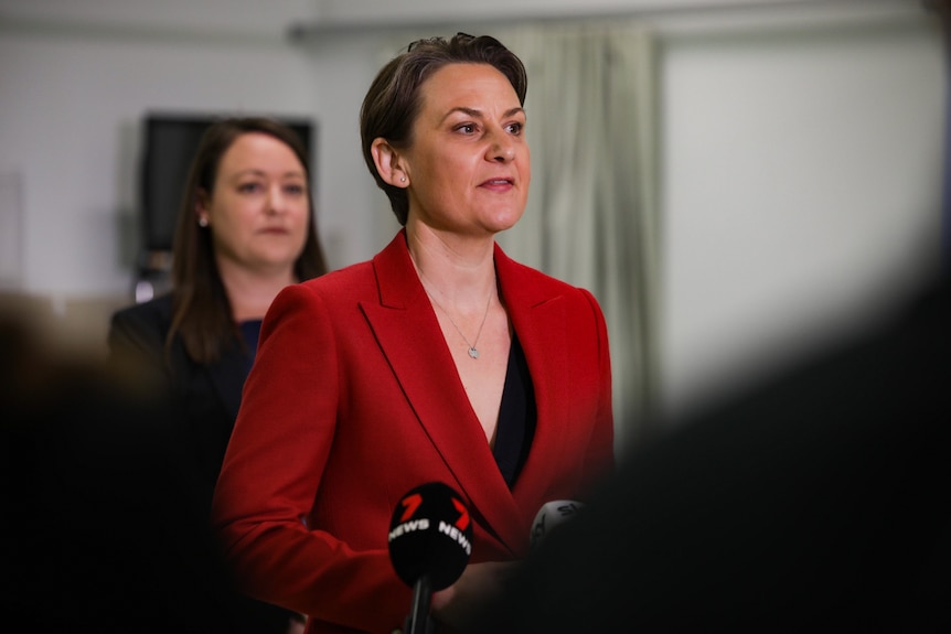 A mid-shot of WA Health Minister Amber-Jade Sanderson speaking at a media conference indoors wearing a red jacket.
