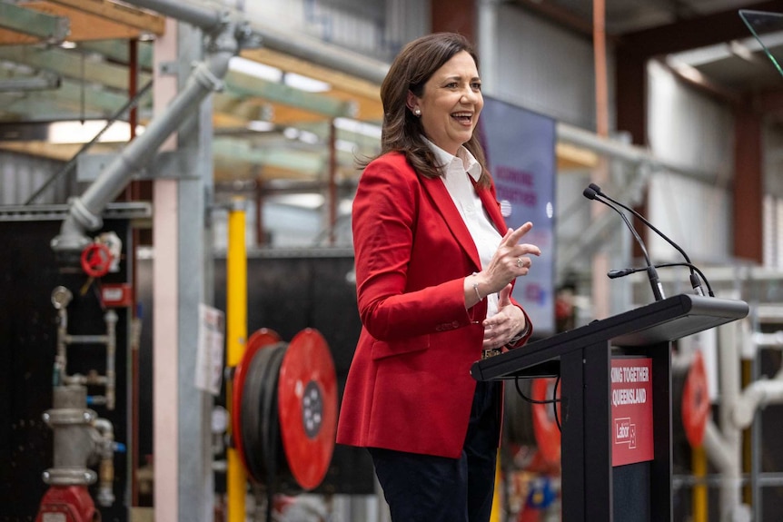 A woman in a red blazer speaks at a podium.