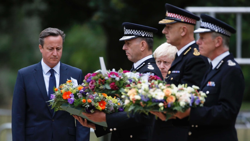 Britain's Prime Minister David Cameron (L) stands with police officers and London Mayor Boris Johnson after laying a wreath at the memorial to victims of the July 7, 2005 London bombings