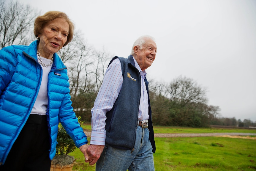 Rosalynn and Jimmy Carter walk hand-in-hand through a green space.