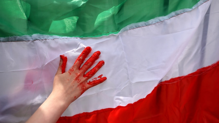 A hand covered in red paint, to look like blood, in front of the Iranian flag