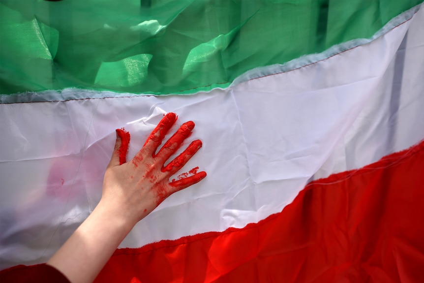 A hand covered in red paint, to look like blood, in front of the Iranian flag