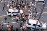 Two New York police cars drive through protesters, who fall to the ground.