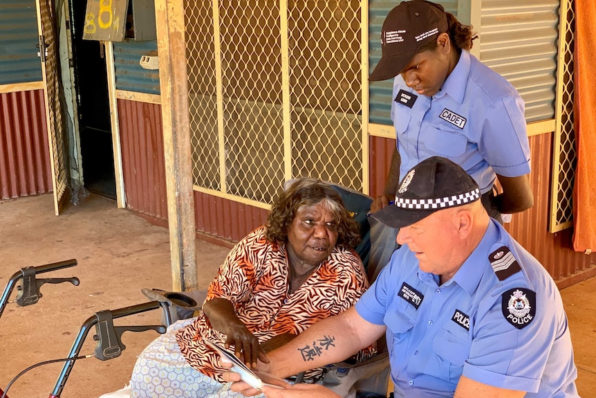 An Aboriginal woman and white man  wearing police uniforms talk to a woman sitting down