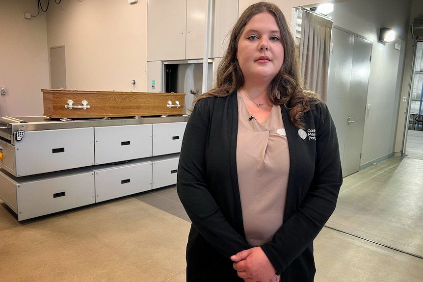 a woman stands with her hands crossed in a funeral home.