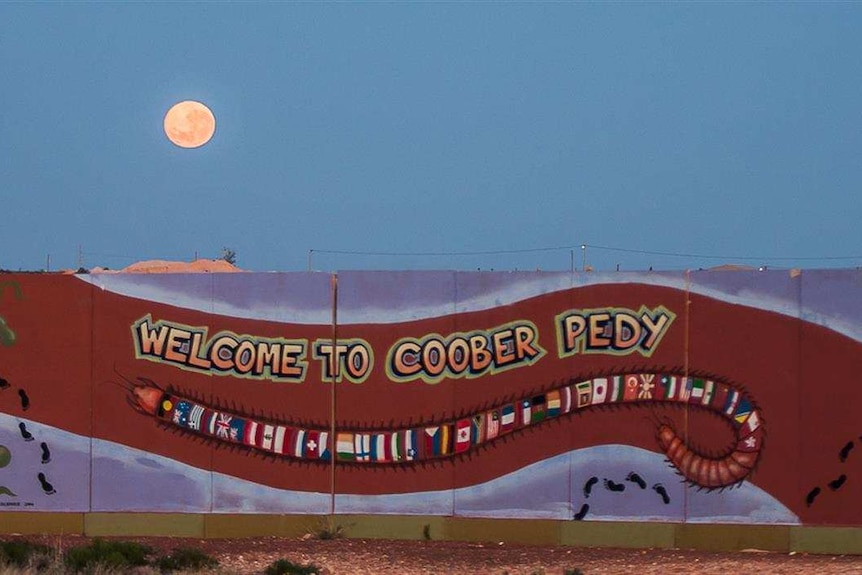 A sign that says Welcome to Coober Pedy and is decorated with Aboriginal art and flags