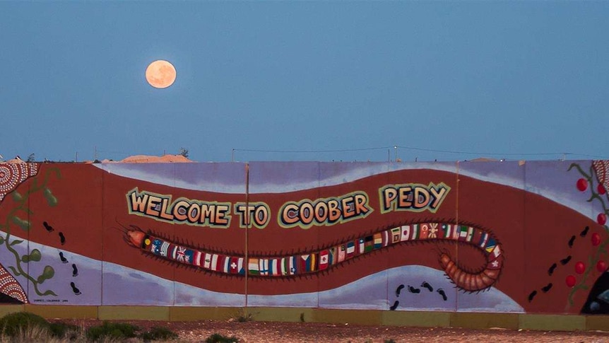 A sign that says Welcome to Coober Pedy and is decorated with Aboriginal art and flags