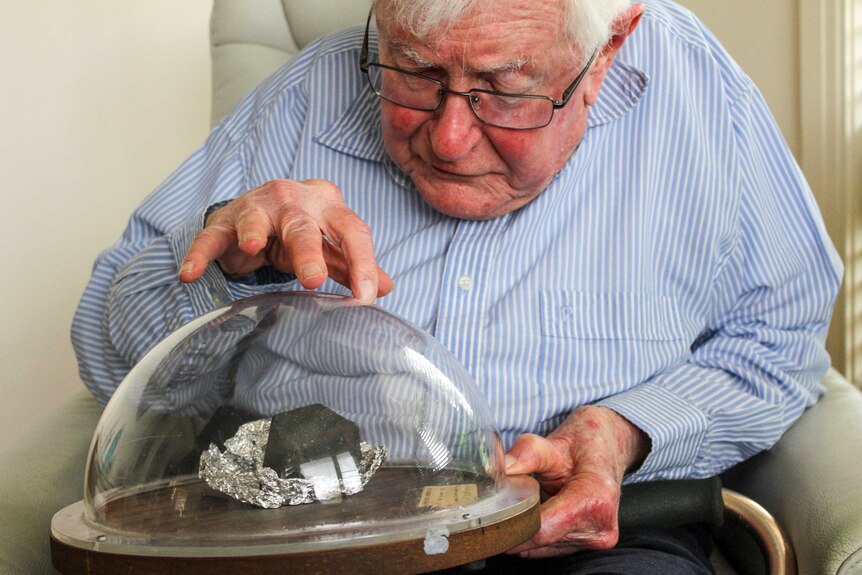 An elderly man pointing out significant aspects of the meteorite sample.
