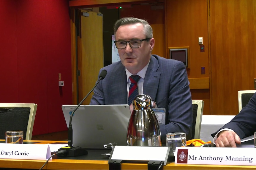 Man with glasses talking into microphone behind desk