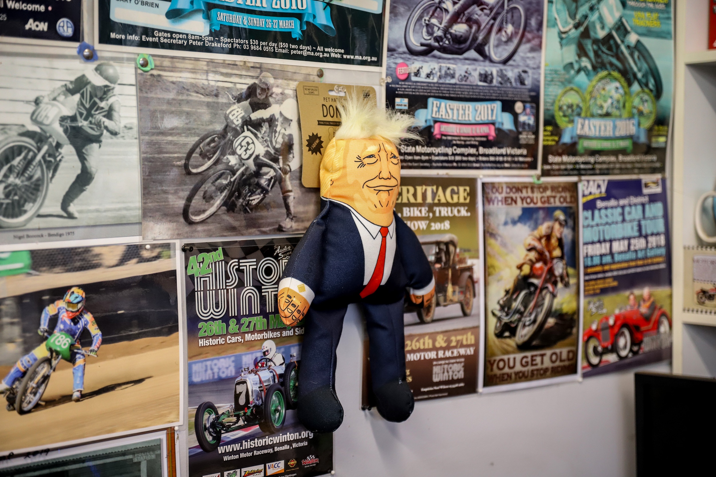 A soft toy doll of Donald Trump pinned to a shop wall with posters behind it.