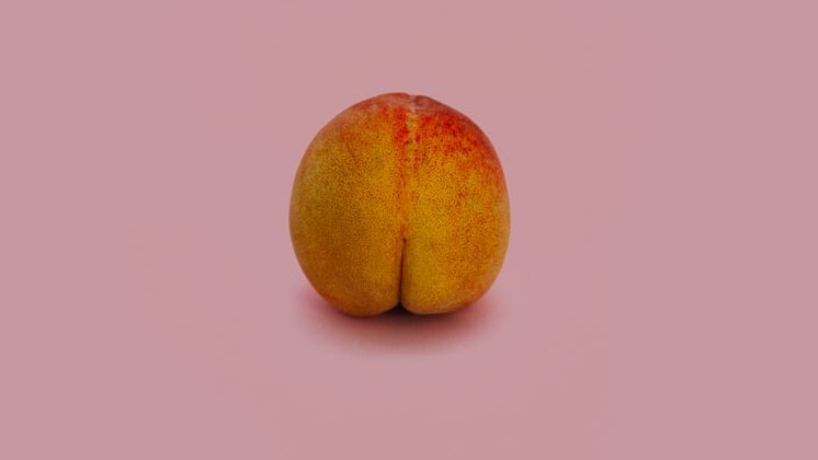 A peach that looks a bit like a bum sits against a pink background