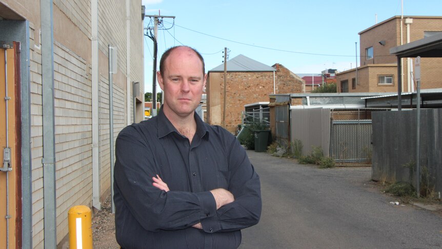 Tall man with arms crossed in a laneway