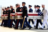 Group of soldiers carry cases draped in US flags