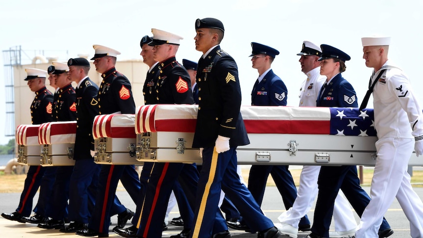 Group of soldiers carry cases draped in US flags