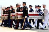 Group of soldiers carry cases draped in US flags