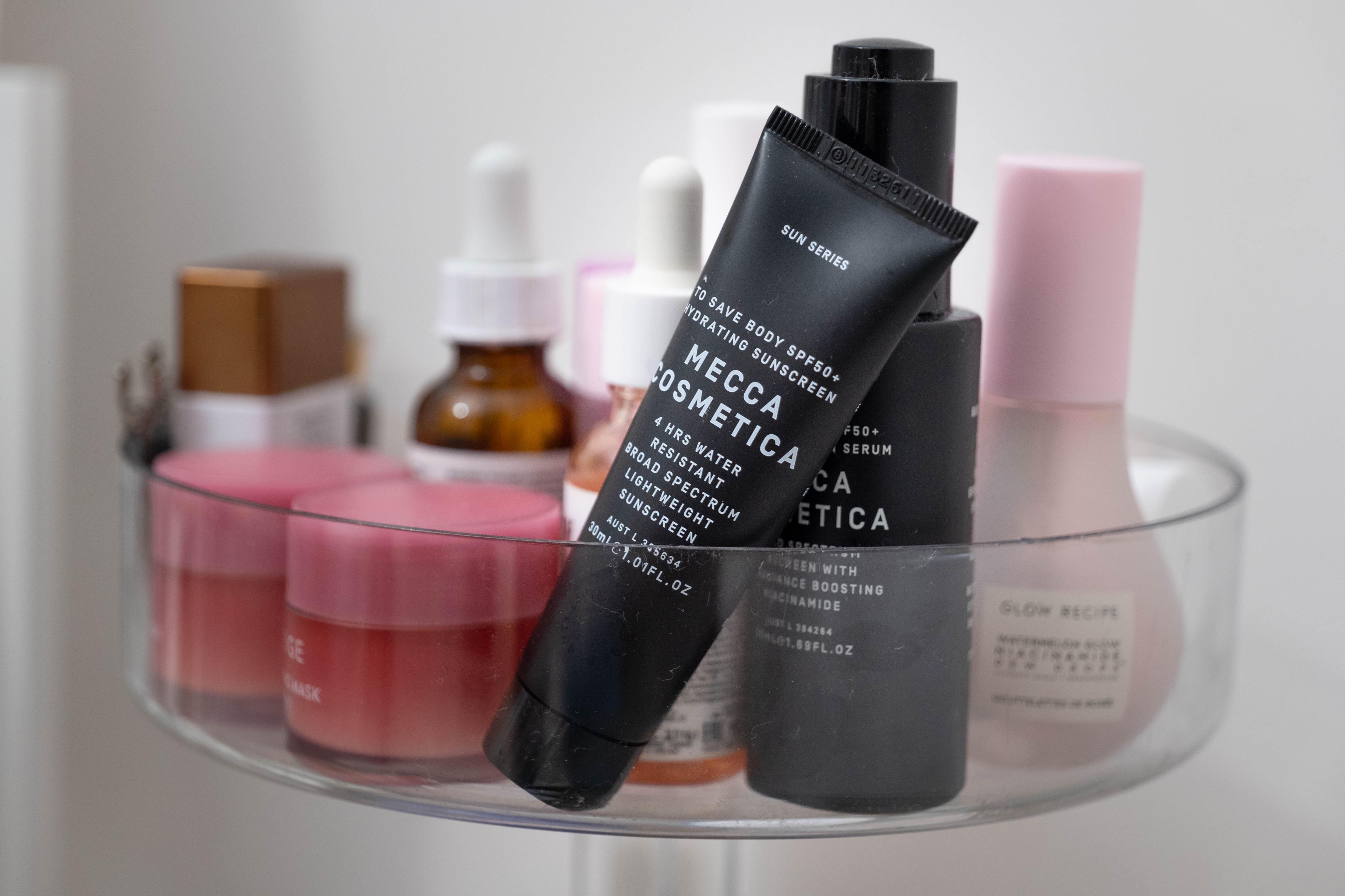 A close up of a clear tray hold a range of beauty products in black tubes and pink glass pots.