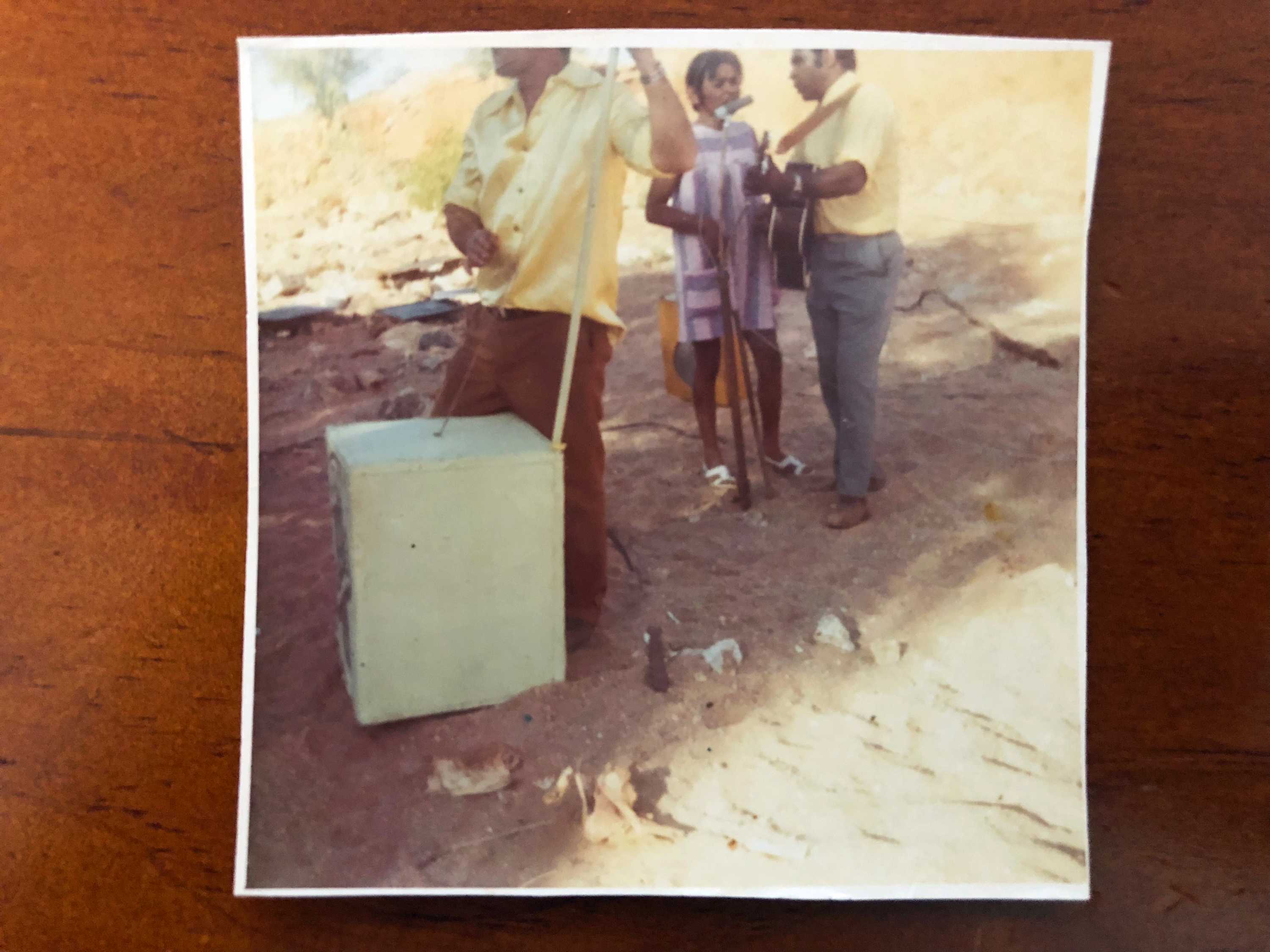 A polaroid image of three people playing instruments in a dry sandy creek bed.