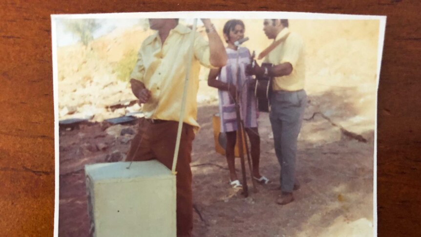 A polaroid image of three people playing instruments in a dry sandy creek bed.