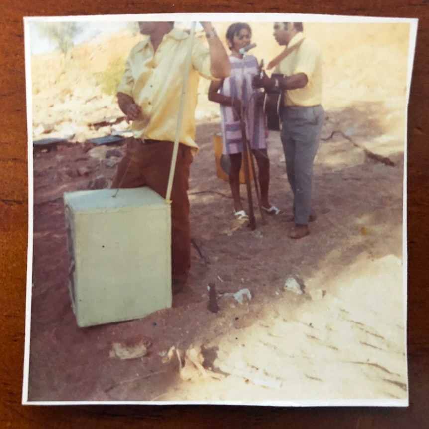 A polaroid image of three people playing instruments in a dry sandy creek bed.