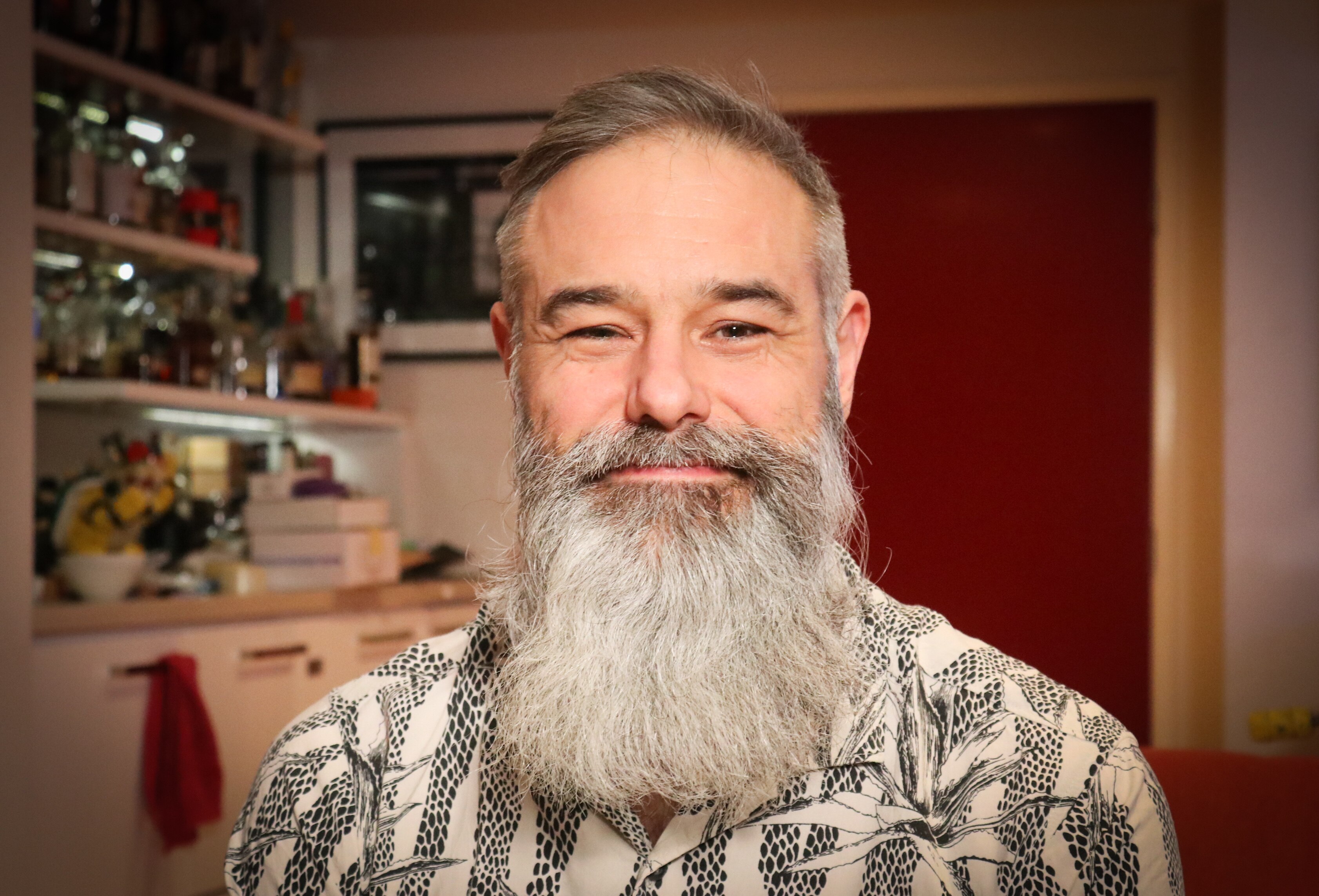 A man with a grey beard in a black and white shirt smiling at the camera