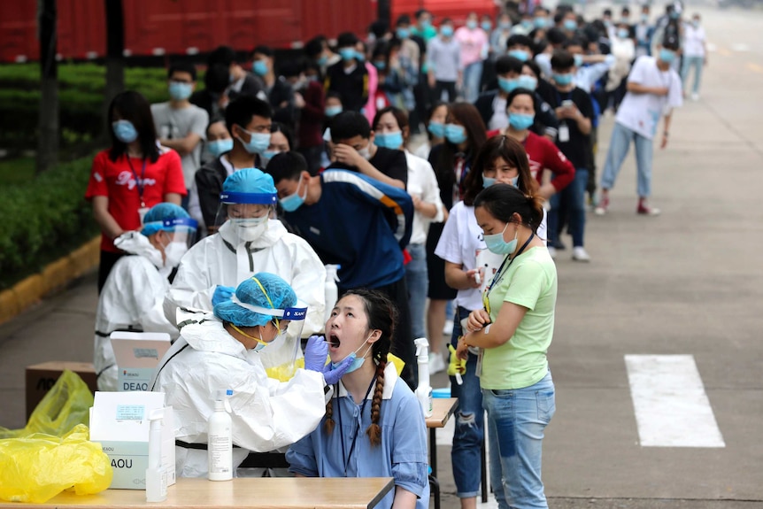 在武汉的一家大型工厂，工人们在医务人员面前排队采集拭子以检测冠状病毒。