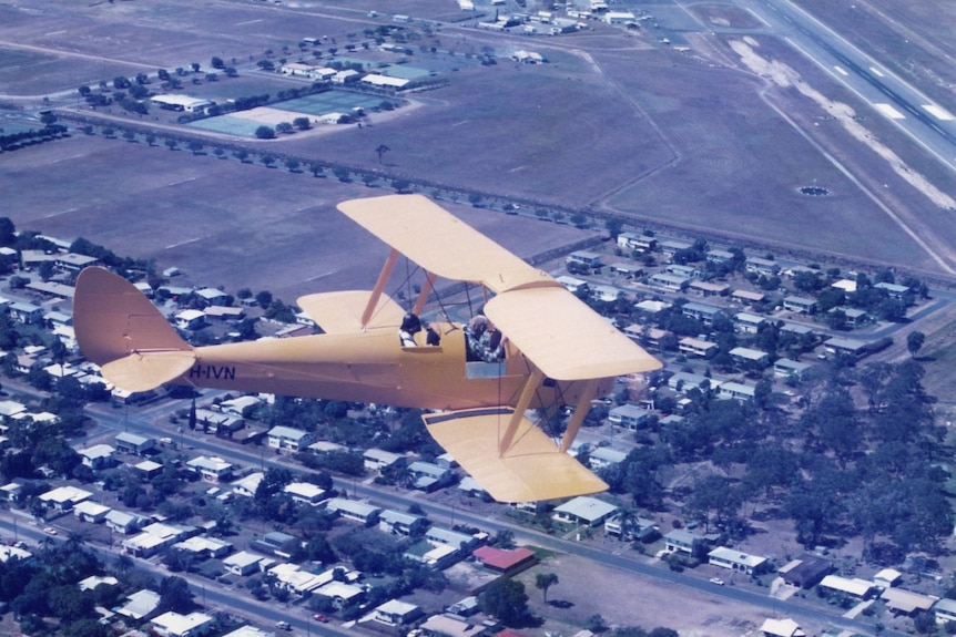 an old yellow plane flying above a town