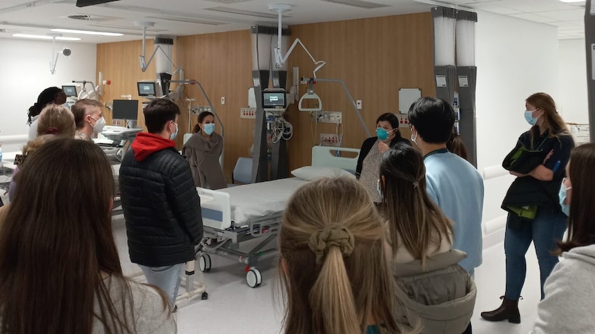 A group of students standing around a hospital bed.