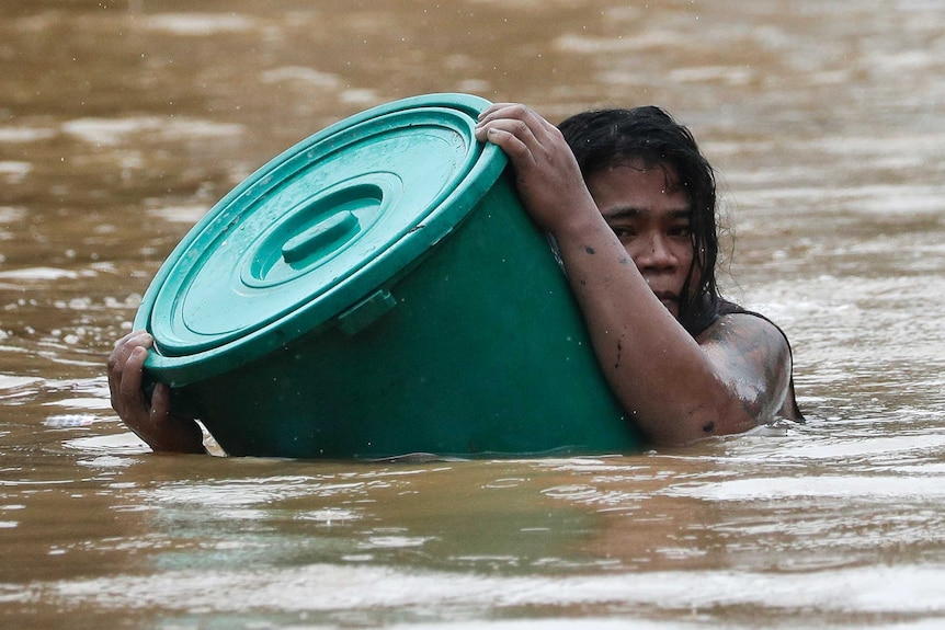 A woman uses a plastic container as a floater while negotiating rising floodwaters