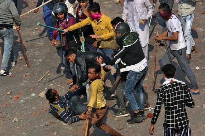 Protesters in the streets of India beating up a man with sticks.